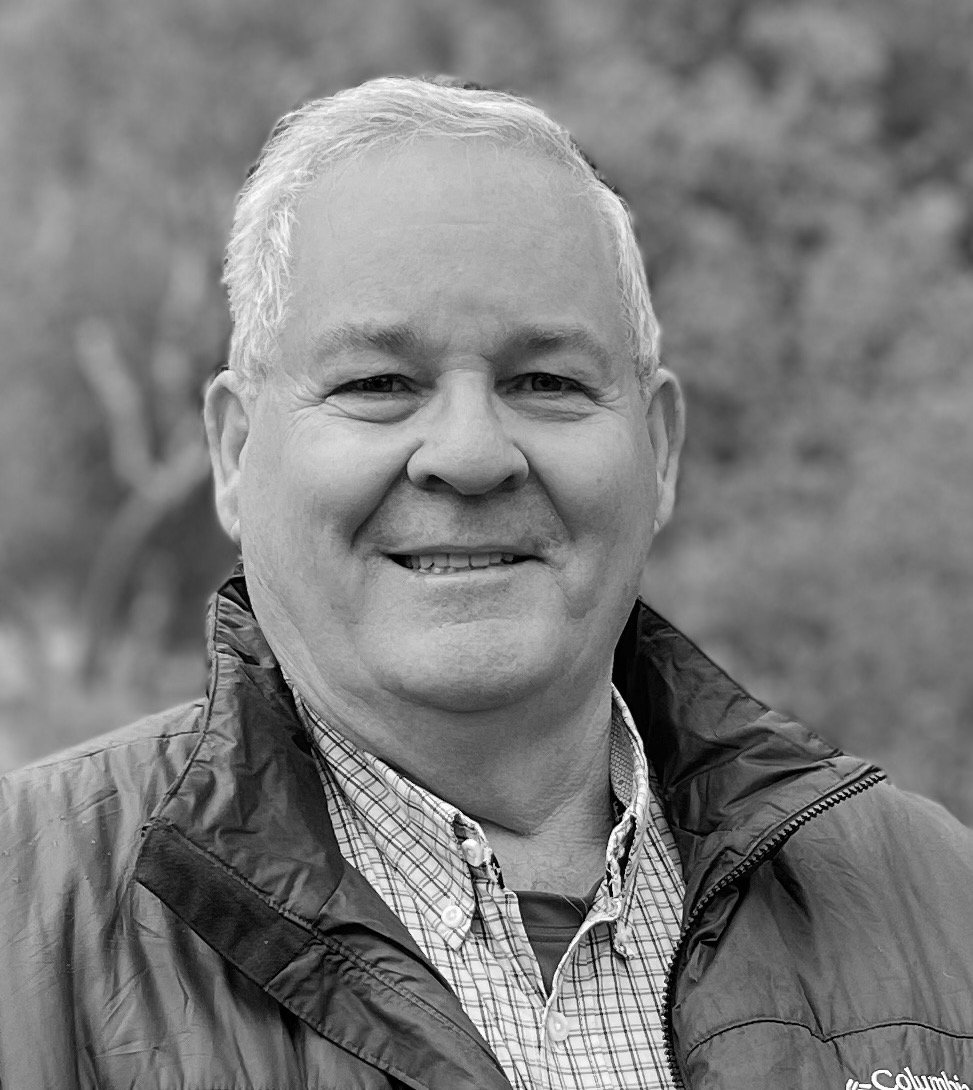 Close up black and white photo of grey haired man smiling wearing a coat.