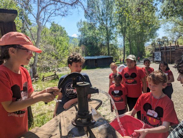 group of kids with hand water pump filling a bucket