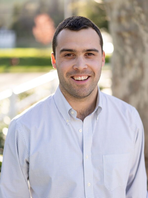 Outdoor photo of man smiling in light dress shirt with tree in background