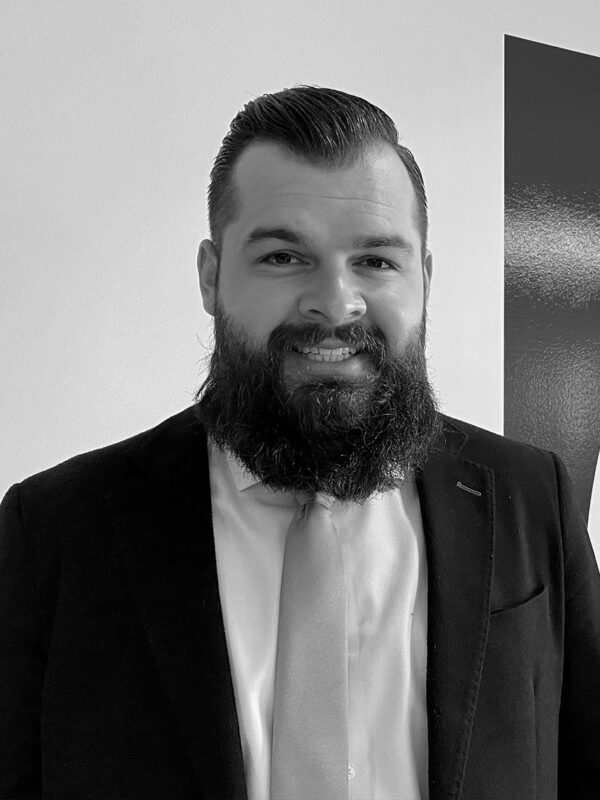 Black and white photo of black haired bearded man in a suit and tie.