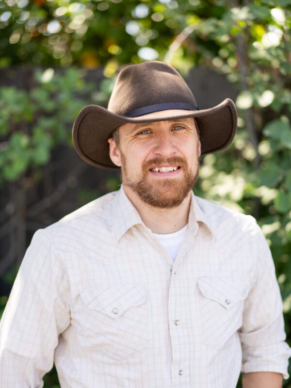 Outdoor photo of man smiling in cowboy hat with leaves in background